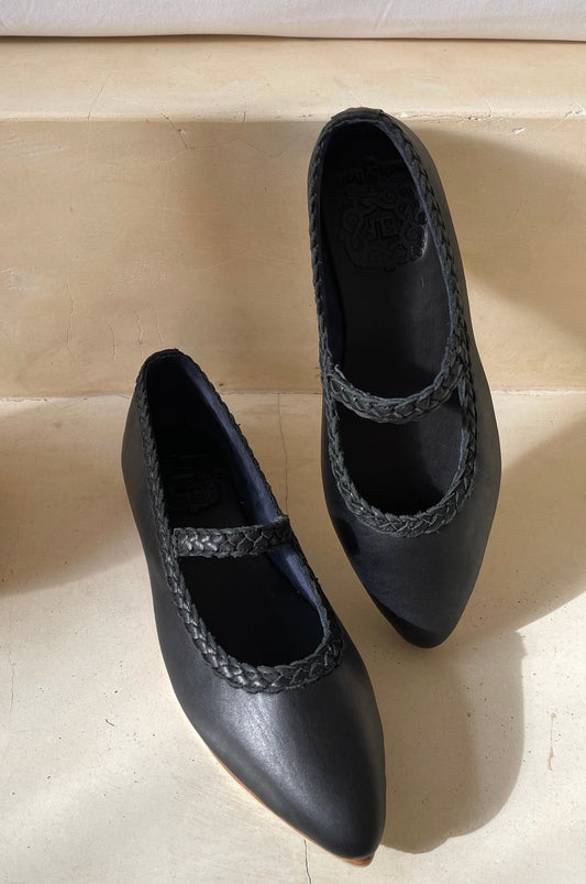 Pair of black shoes with braided details on a light wooden floor.