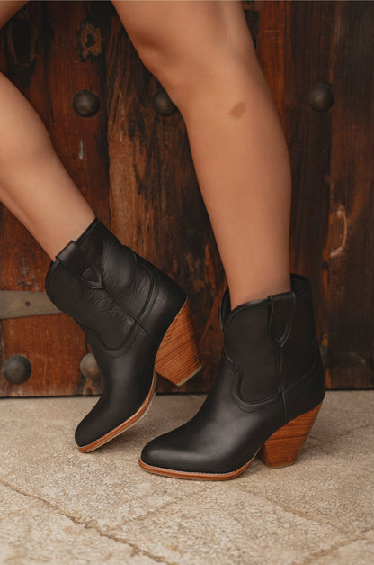 Black ankle boots with wooden soles worn by a person on a stone floor.