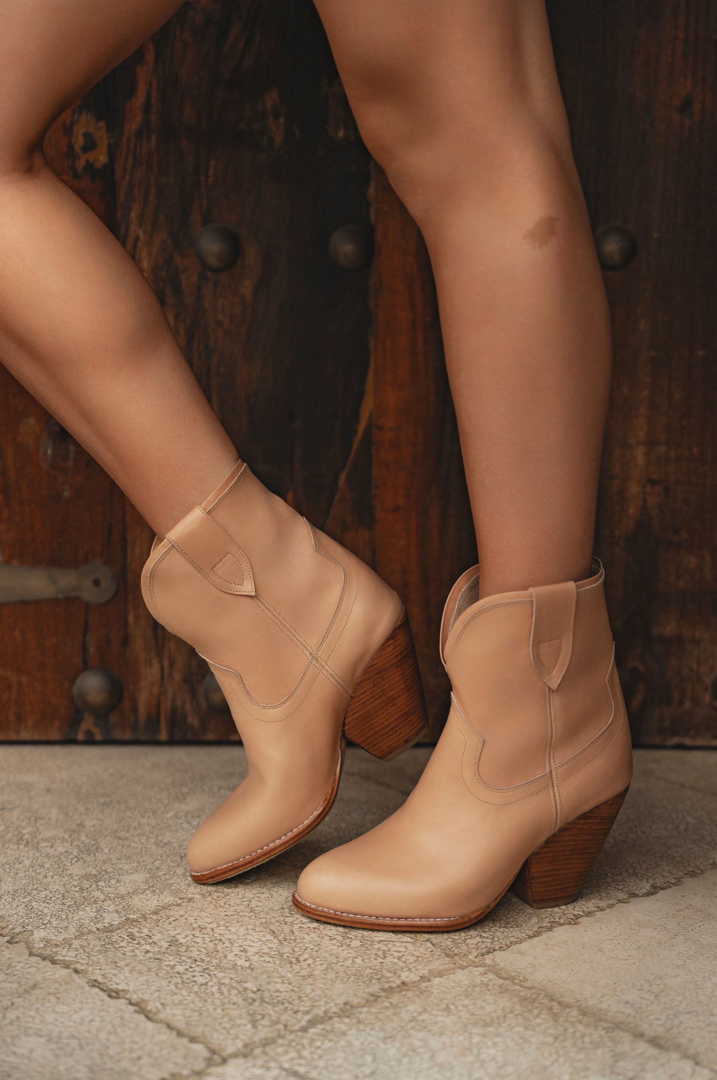Tan cowboy boots worn by a person on a stone floor with a wooden door in the background