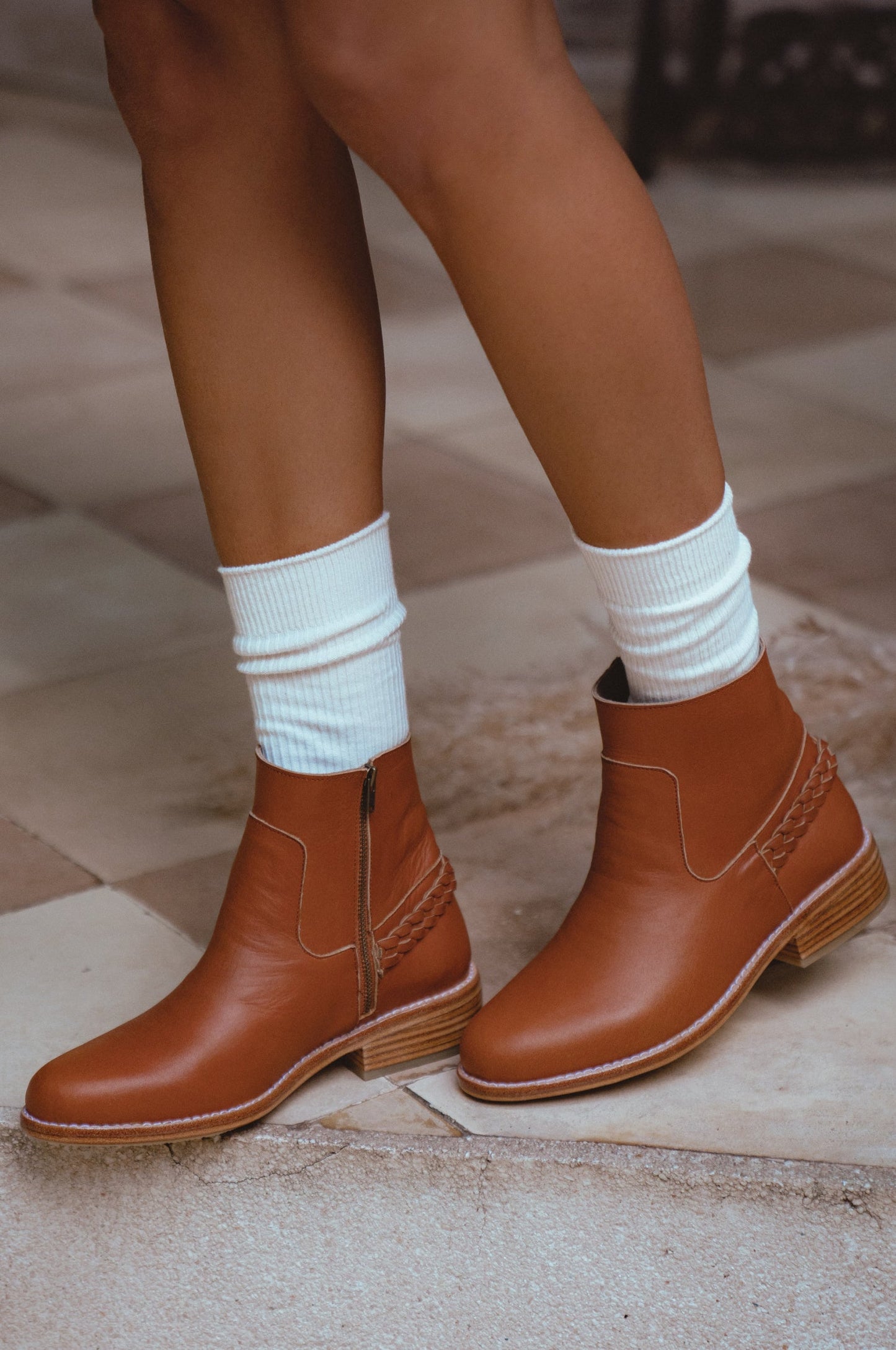 Brown ankle boots worn with white socks on a stone floor.