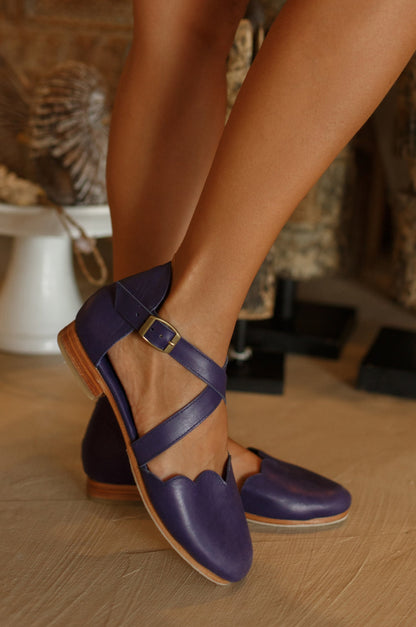 Purple shoes with brown soles worn by a person on a wooden floor.