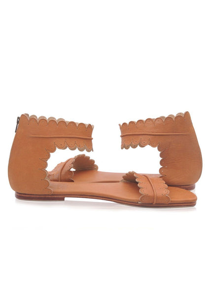 Pair of tan sandals with scalloped edges on a white background