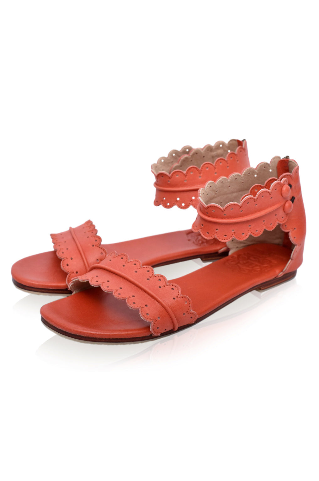 Pair of red sandals with scalloped edges on a white background