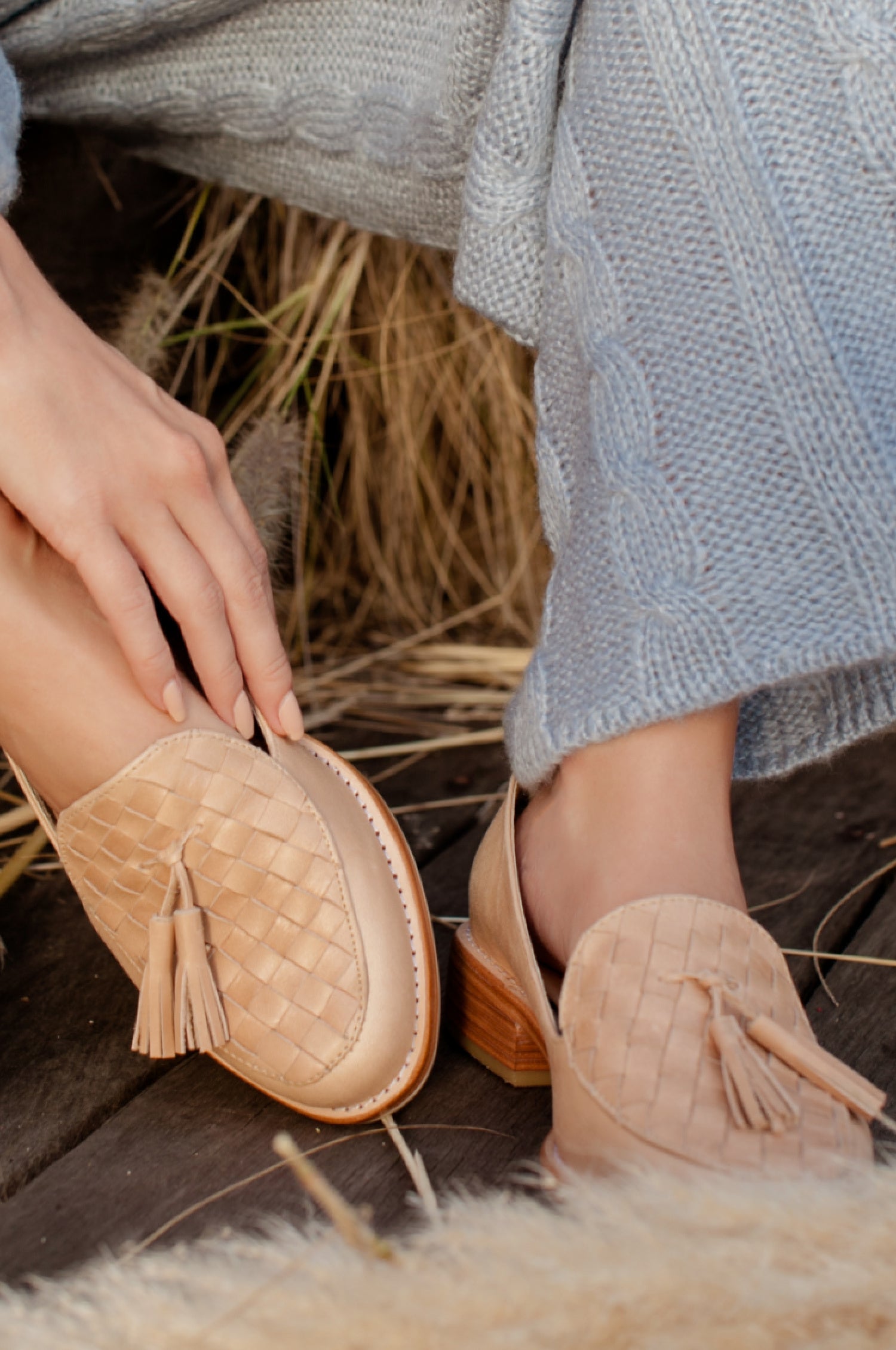 Person wearing beige woven shoes with tassels on a wooden floor.