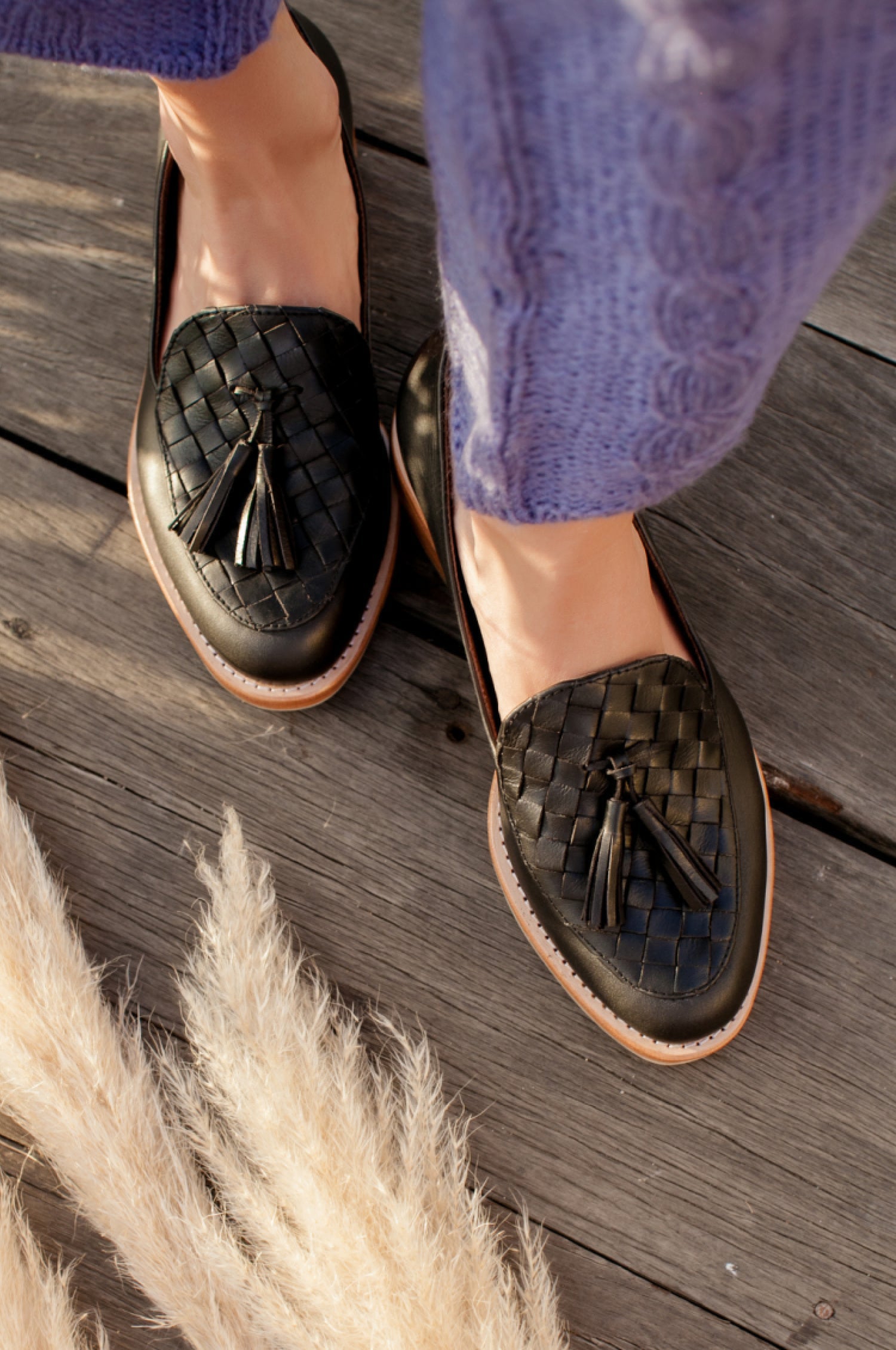 Woven loafers with tassels worn by a person on a wooden floor.