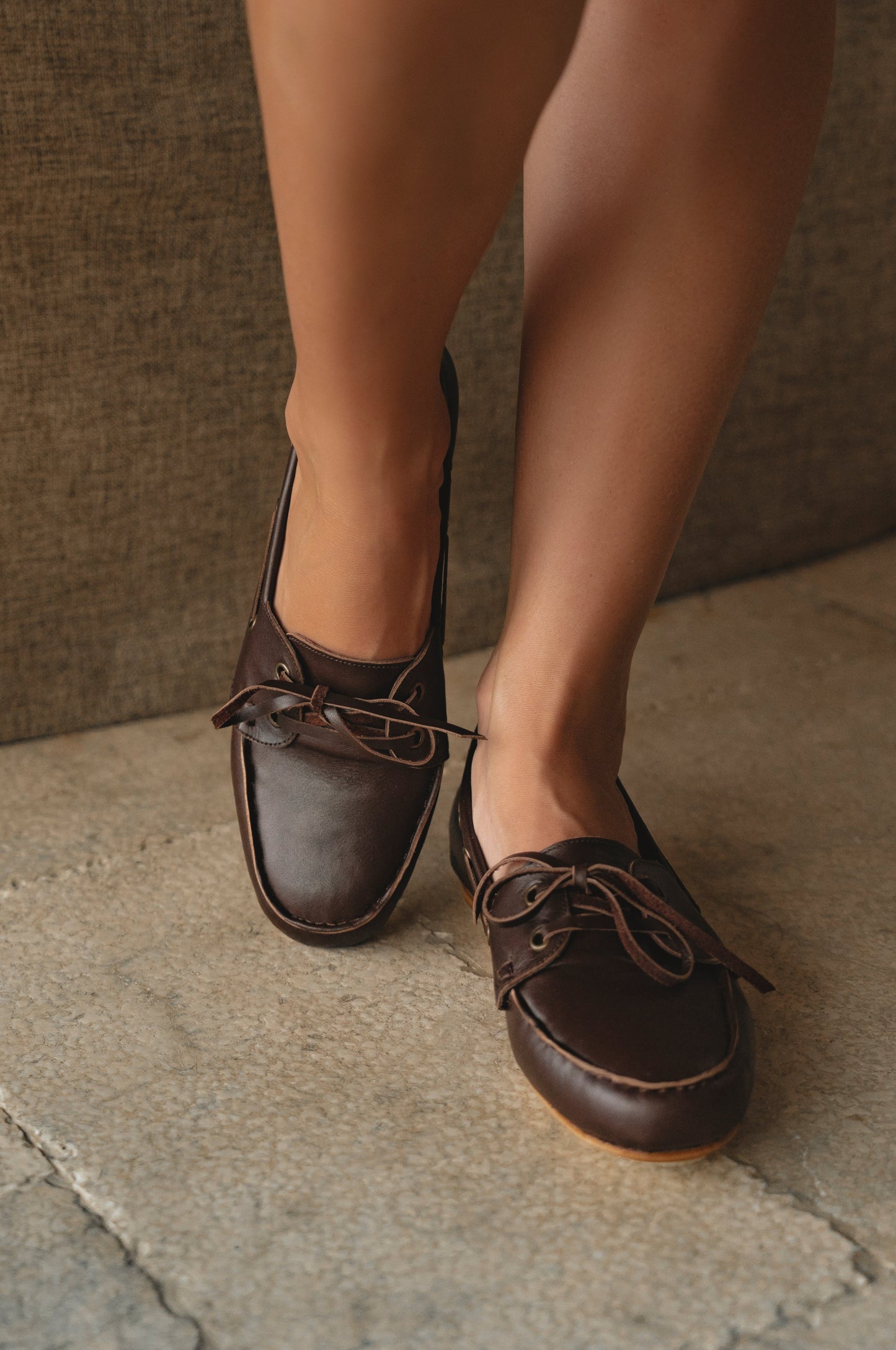 Brown leather shoes worn by a person on a stone floor.
