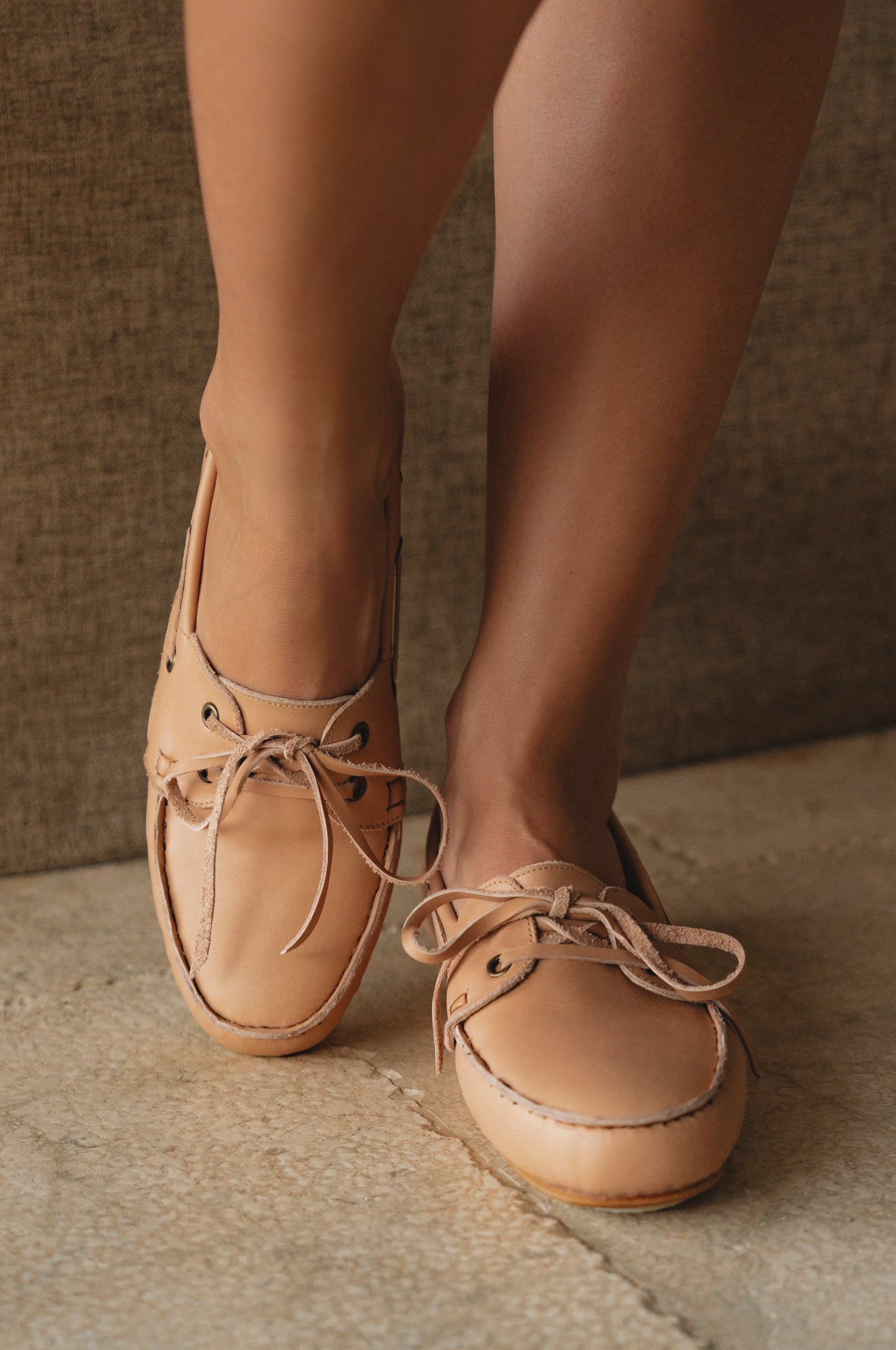 Tan leather shoes worn by a person on a textured surface with a neutral background