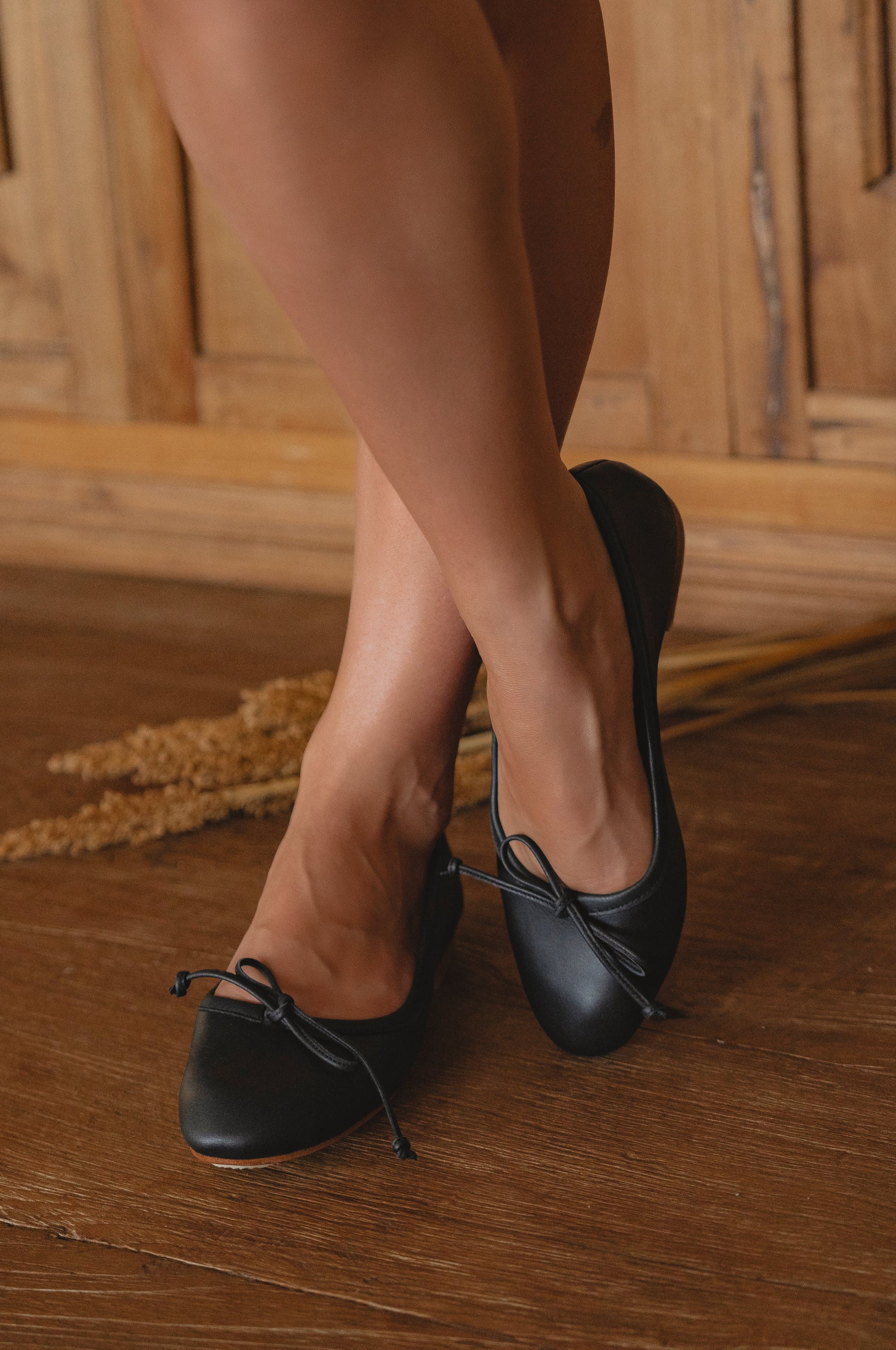 Black ballet flats worn on a wooden floor with a neutral background