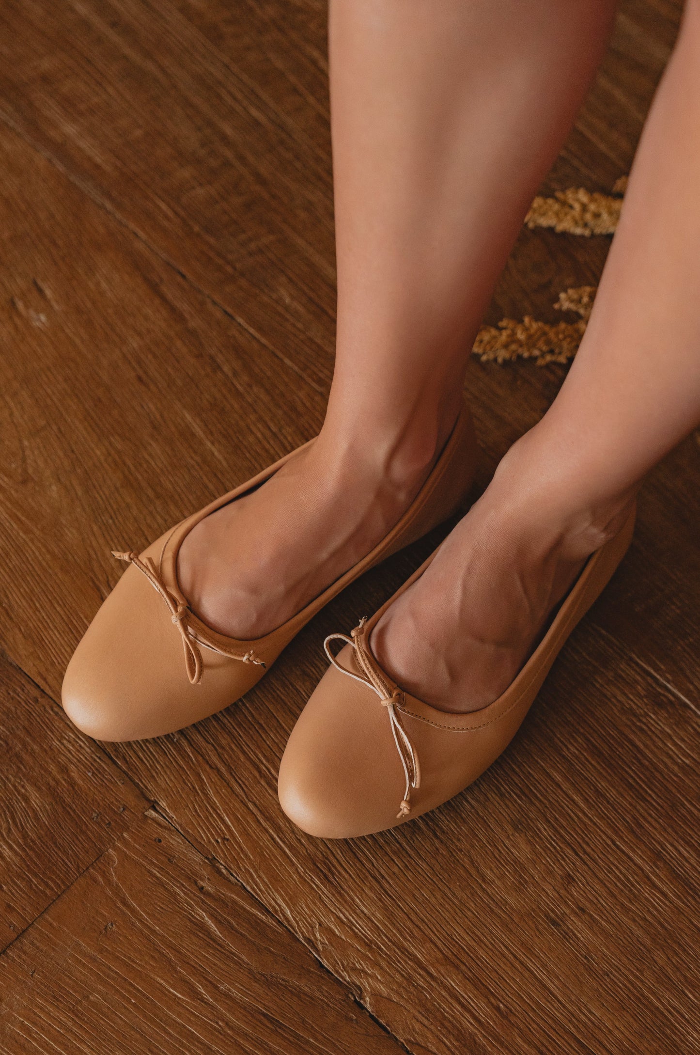 Tan ballet flats worn on a wooden floor
