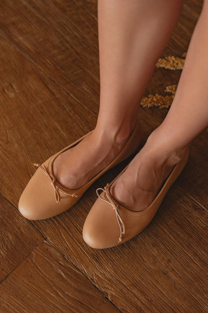 Tan ballet flats worn on a wooden floor