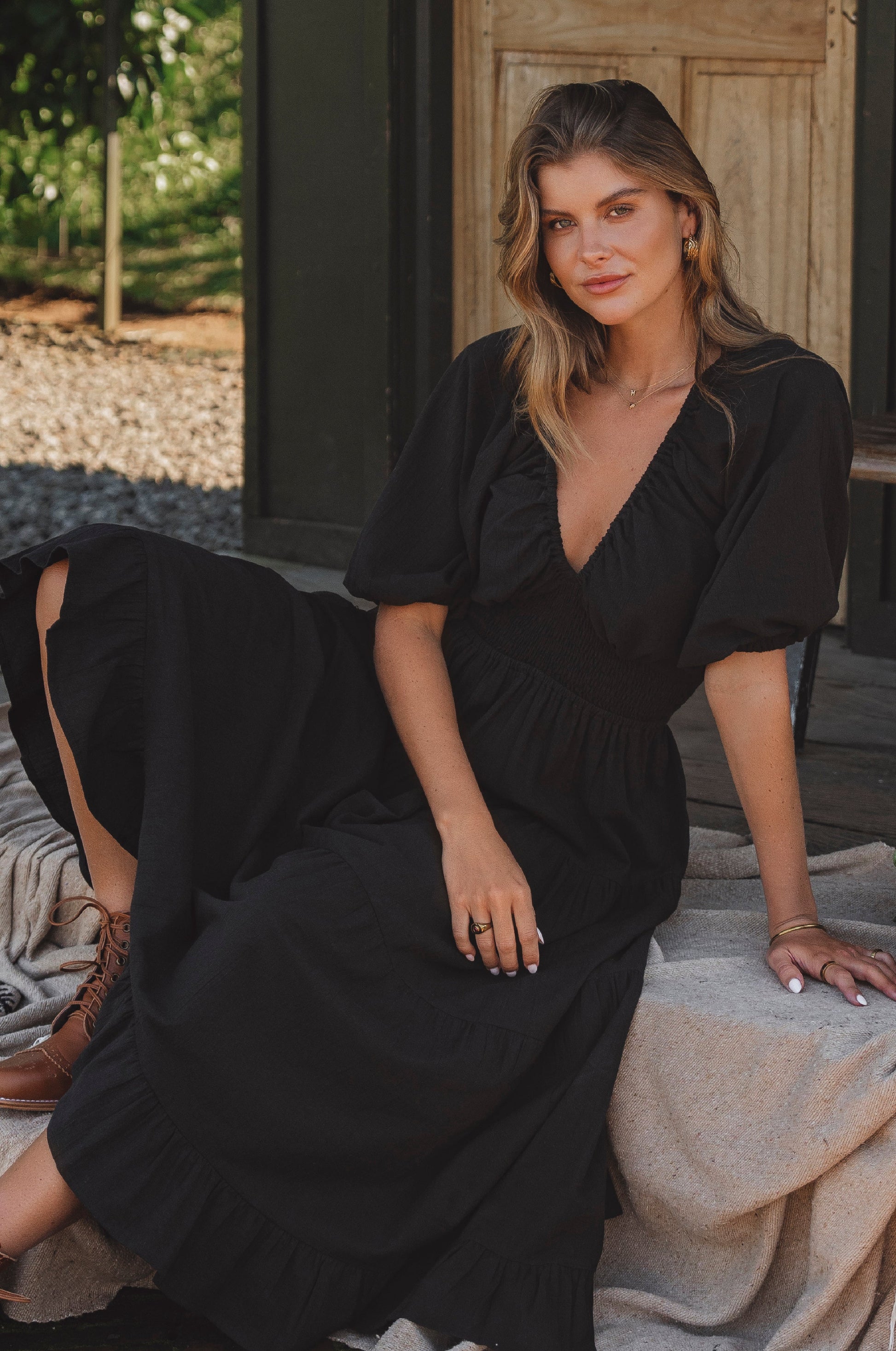 Woman in a black dress sitting outdoors with a wooden door in the background