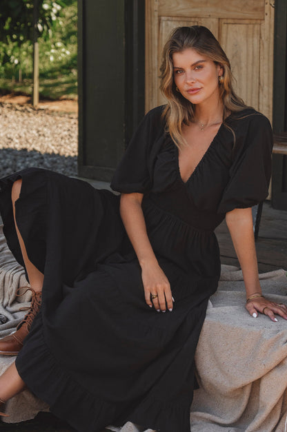 Woman in a black dress sitting outdoors with a wooden door in the background