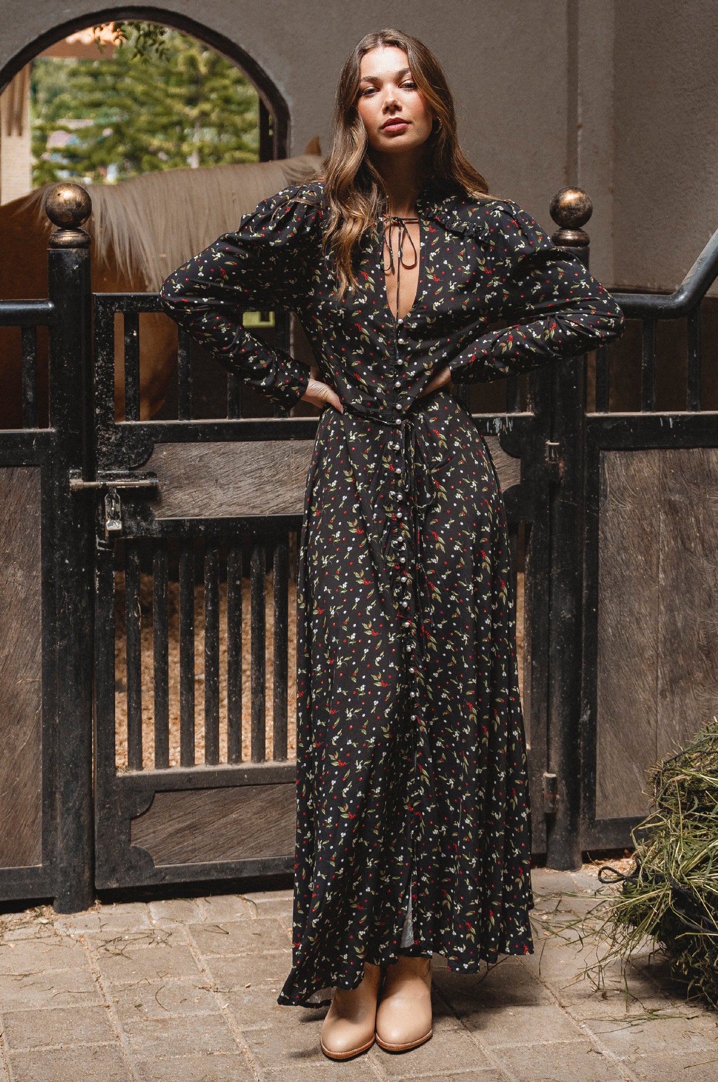 Woman in a black floral dress standing in front of a wooden gate.