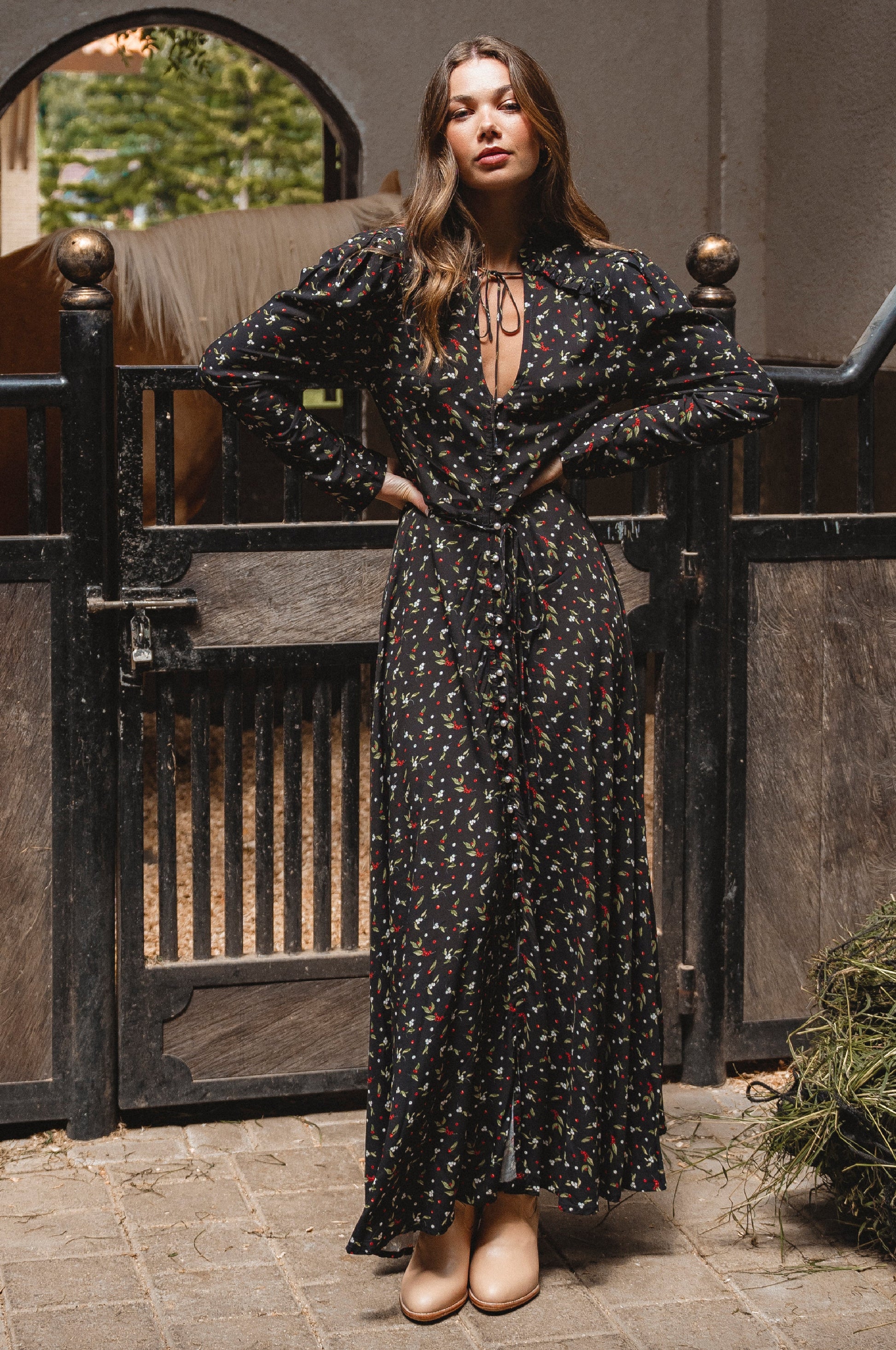 Woman in a black floral dress standing in front of a wooden gate.