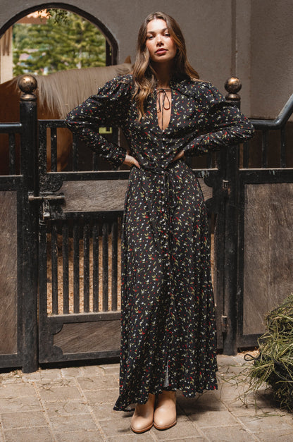 Woman in a black floral dress standing in front of a wooden gate.