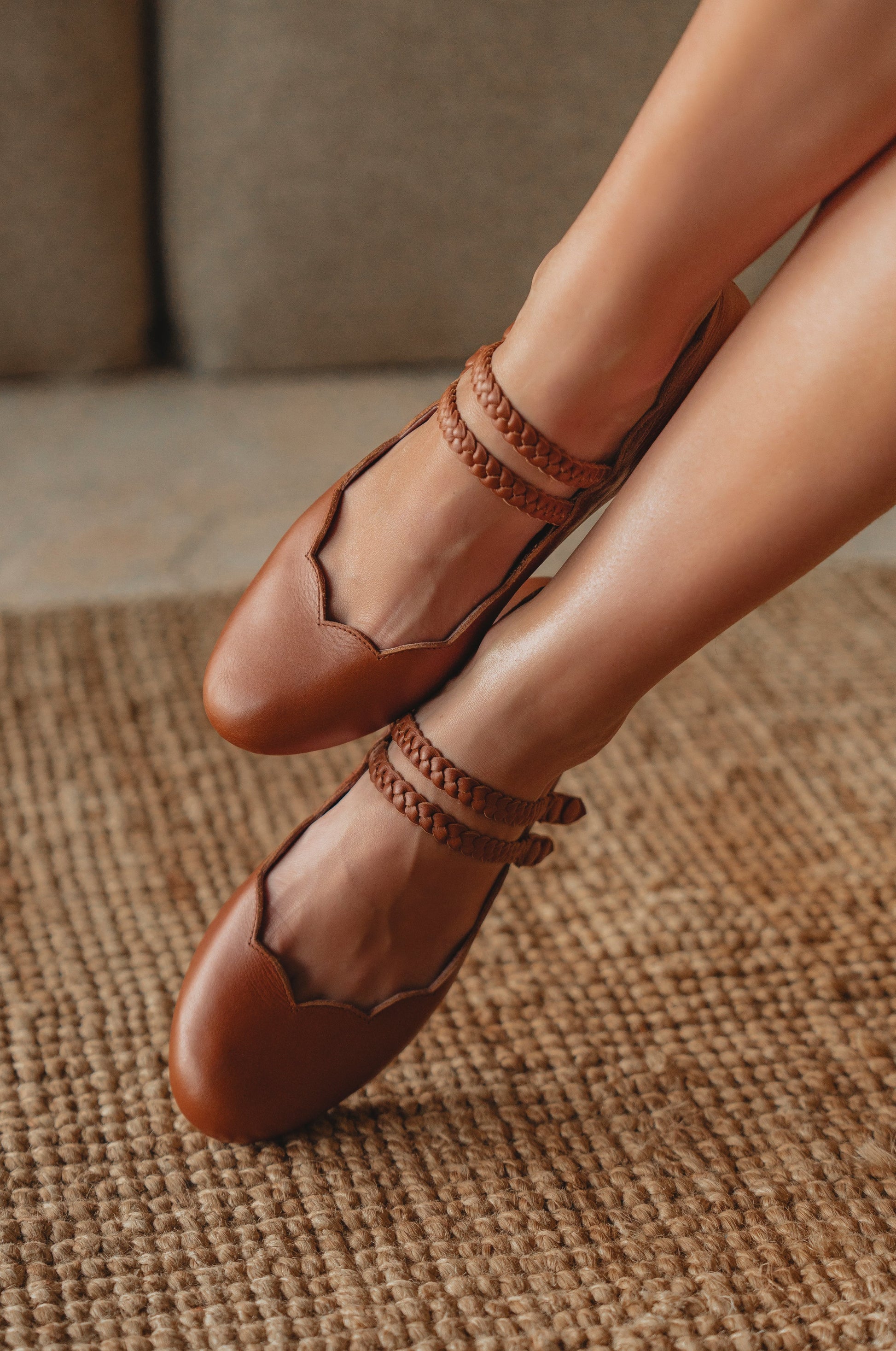 Brown leather shoes with braided straps worn by a person on a textured surface.