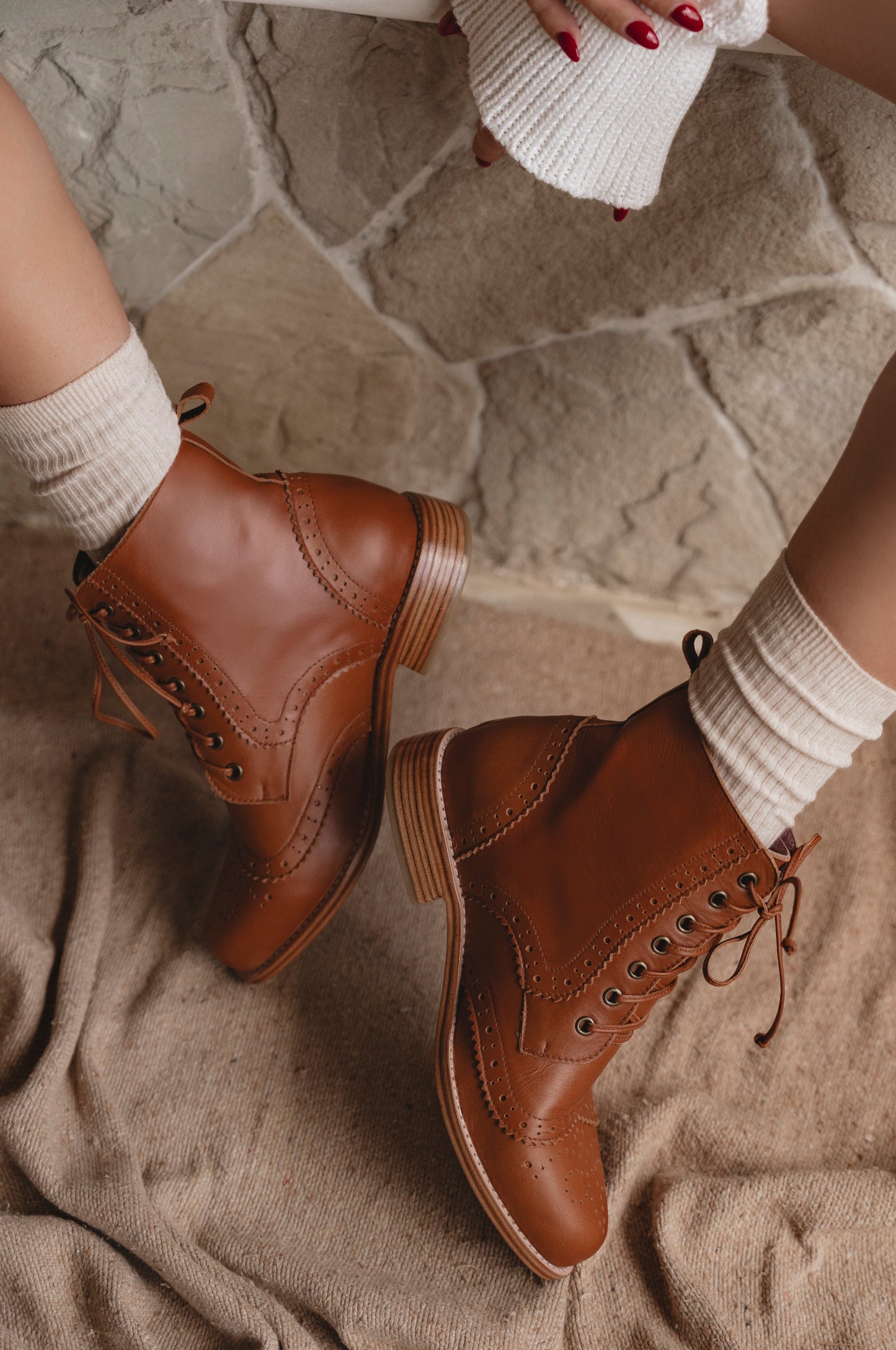 Brown leather boots worn with white socks on a stone floor.