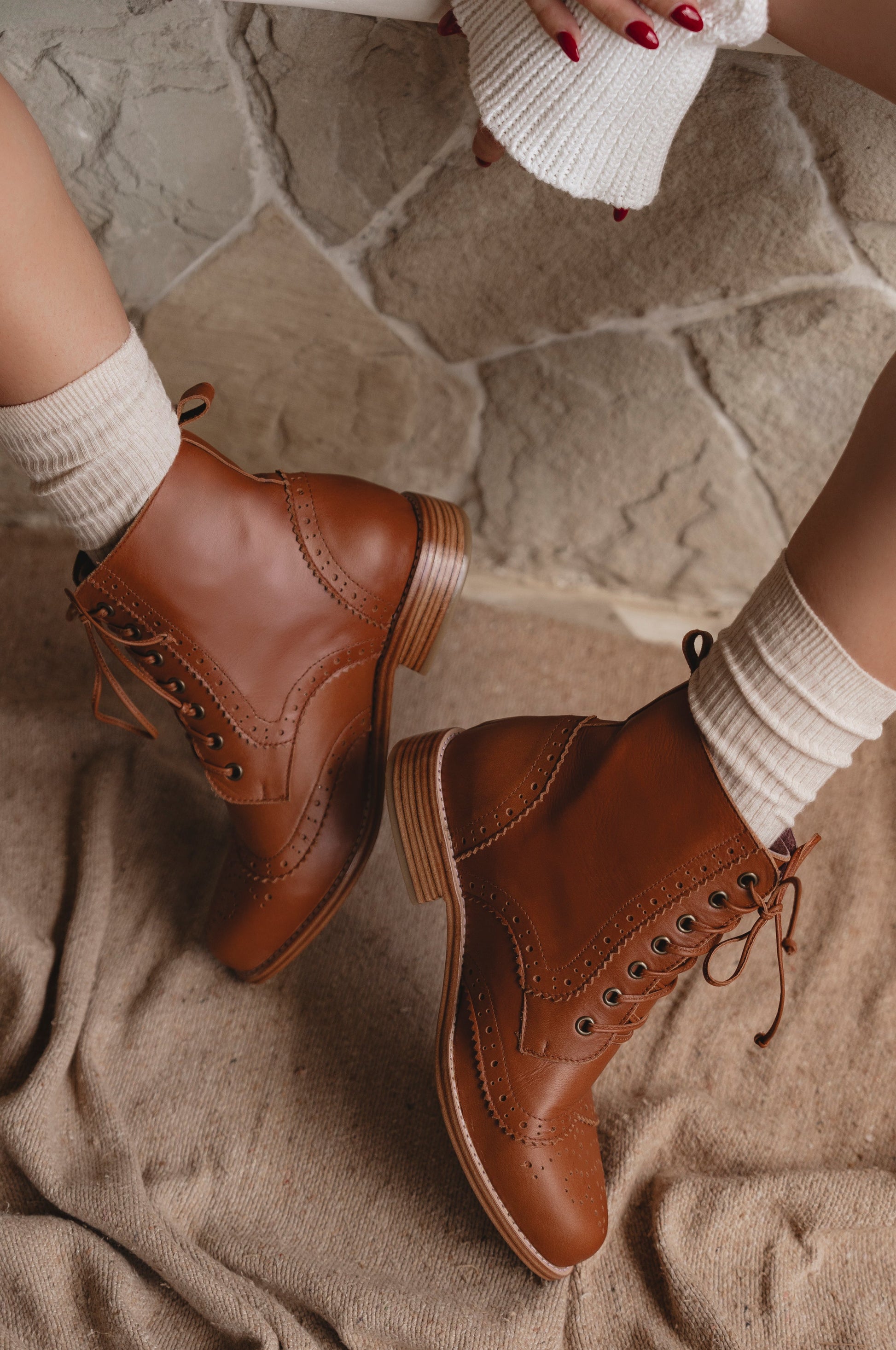 Brown leather boots worn with white socks on a stone floor.