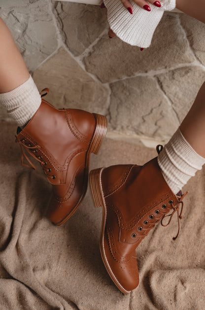 Brown leather boots worn with white socks on a stone floor.