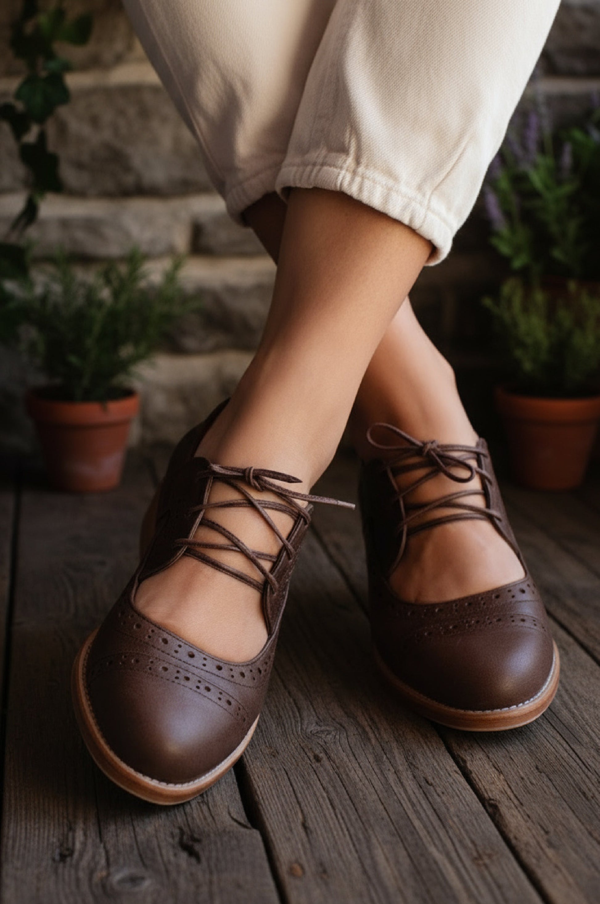 Brown lace-up shoes worn with beige pants on a wooden floor with plants in the background