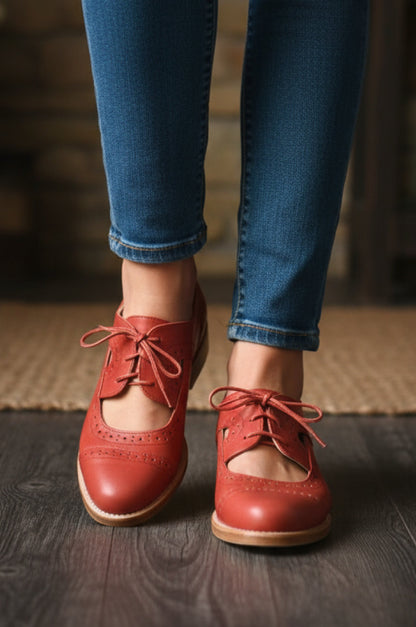 Red brogue shoes worn with blue jeans on a wooden floor.