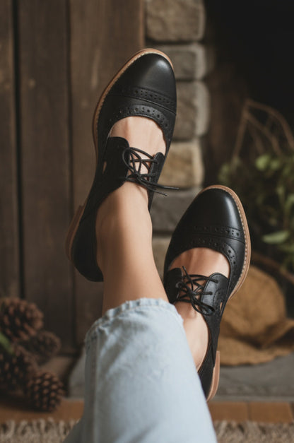 Black shoes with brown soles worn by a person sitting on steps.