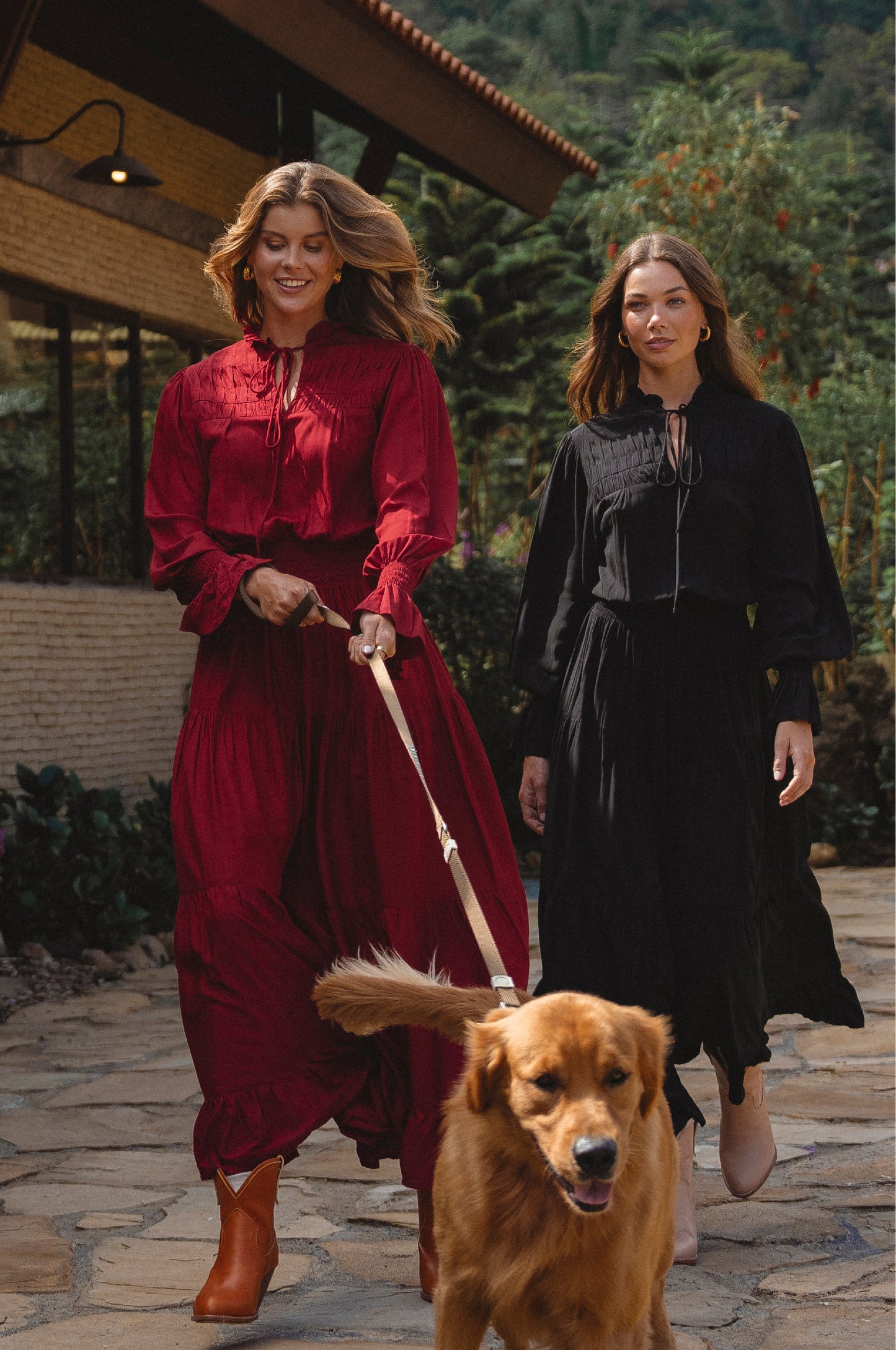 Two women walking a dog on a stone path with a building and trees in the background