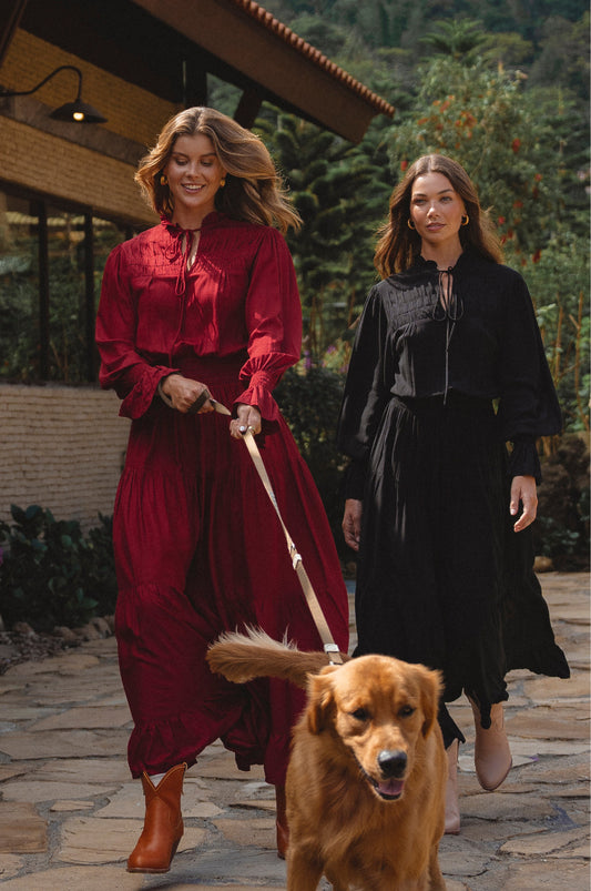 Two women walking a dog on a stone path with a building and trees in the background